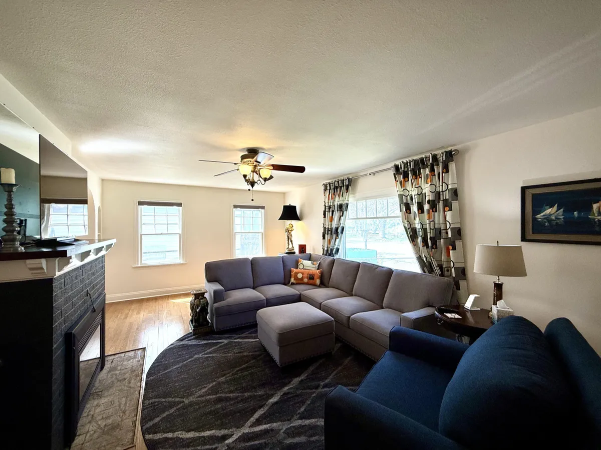 A spacious living room anchored by a large sectional sofa adorned with decorative pillows, positioned near a gas fireplace. Ambient lighting from a floor lamp and soft curtains adds to the cozy ambiance, while the generous seating arrangement makes the space ideal for movie nights or group gatherings.