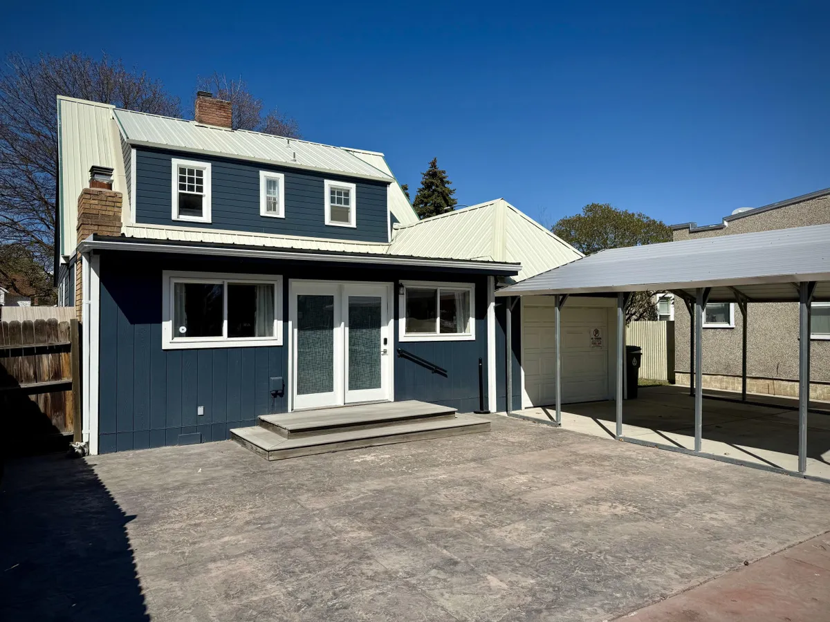 This exterior image captures the blue house with large windows, front steps, and a carport. The scene is lively and cheerful, suggesting the possibility of family gatherings, outdoor barbecues, and children playing in the yard.