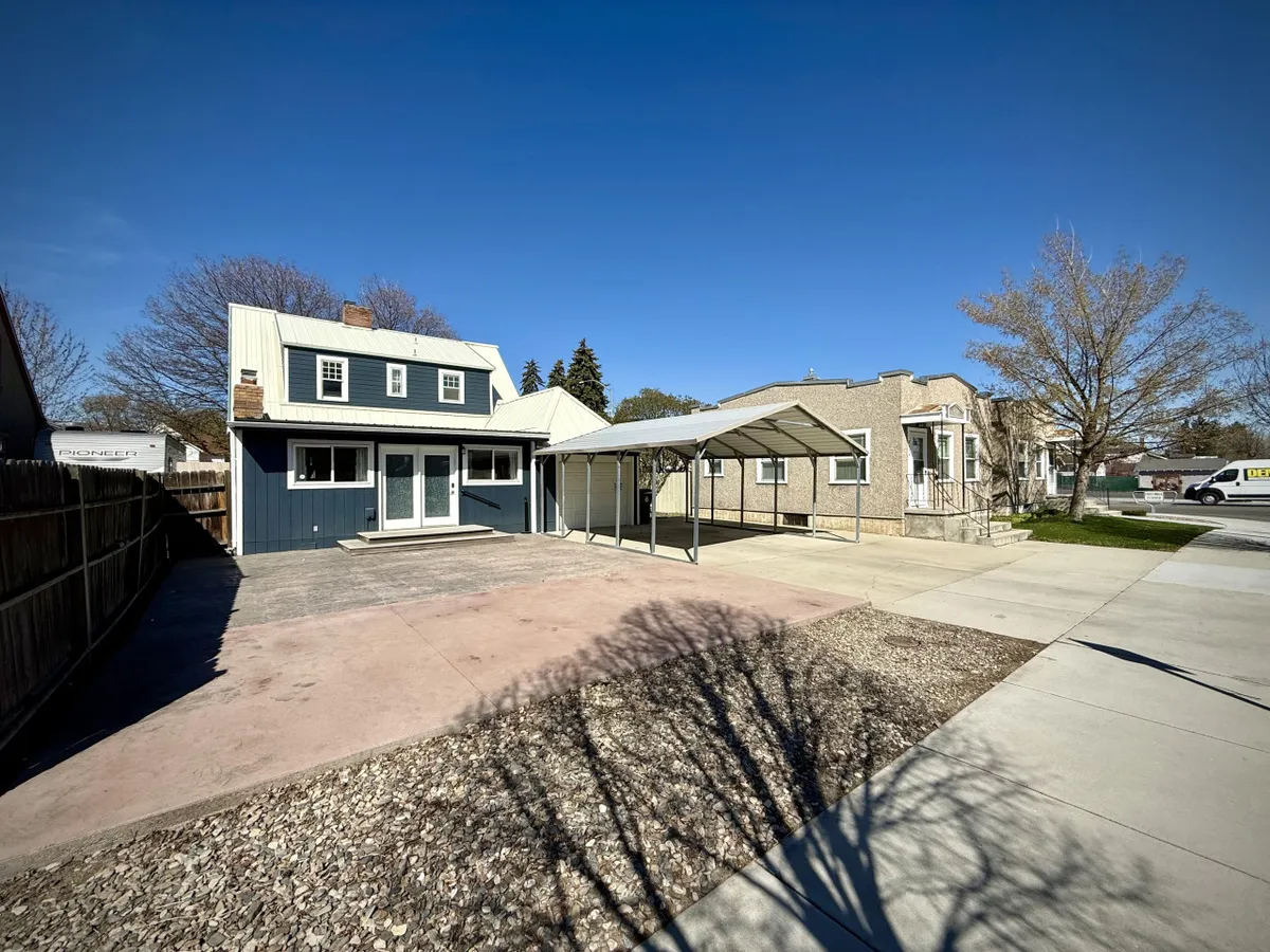 A welcoming exterior view of a two-story house with a carport and a landscaped yard. The scene is alive with imagined family gatherings, outdoor barbecues, and children playing in the sunlit yard. The front of the home feels approachable and hints at the easy access to outdoor spaces.