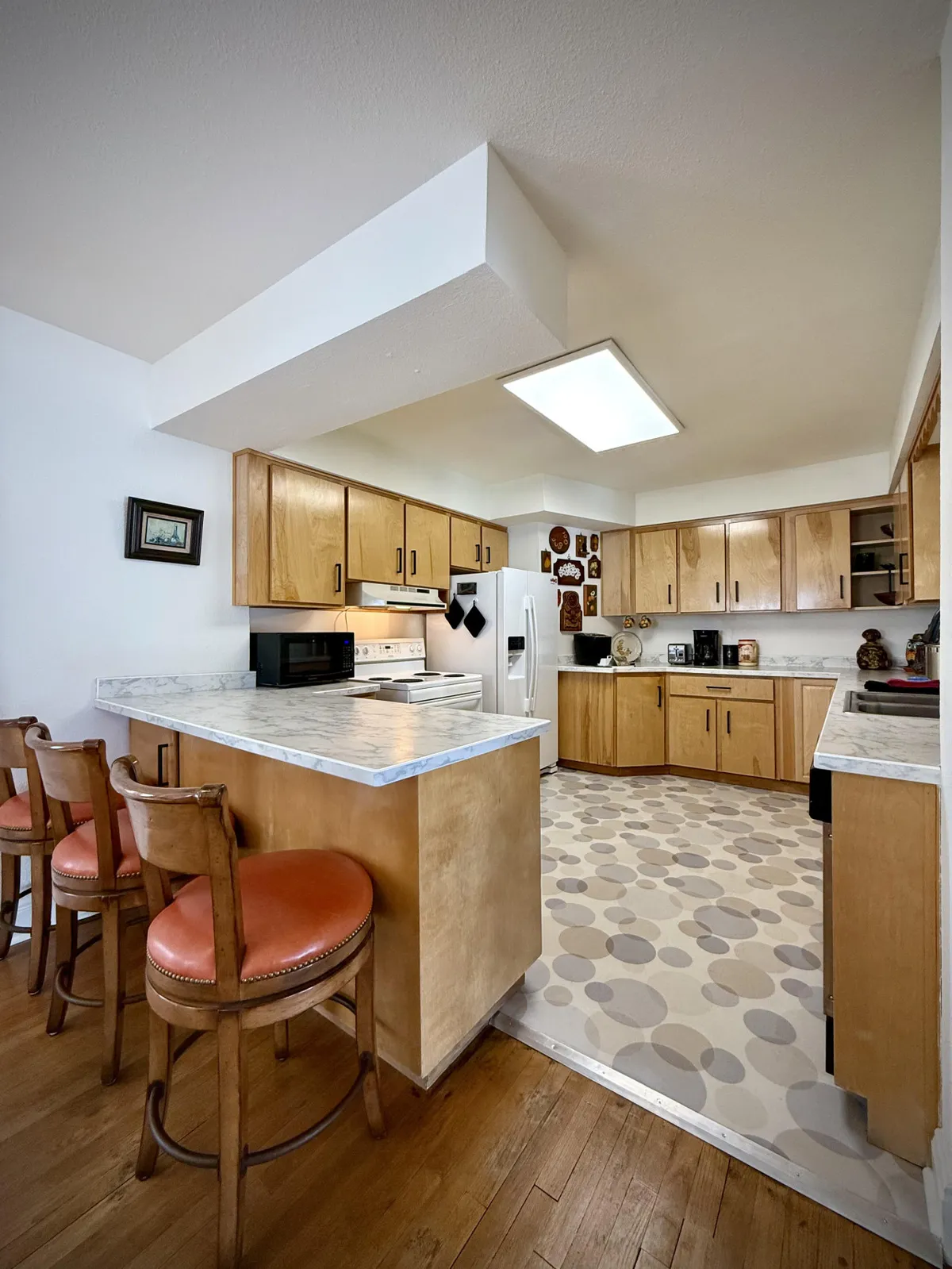 A warm, inviting kitchen with a central island and bar stools, decorative plates on the wall, and modern appliances. The layout encourages both cooking and casual gathering, with ample counter space and seating for guests or family to join in meal prep or conversation.