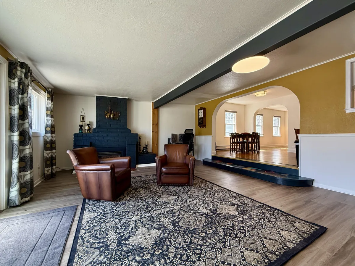 This interior shot features a cozy living area with leather armchairs, a fireplace, an area rug, and a partial view into a dining space. The setup conveys a warm, inviting atmosphere ideal for relaxing with family—including pets.