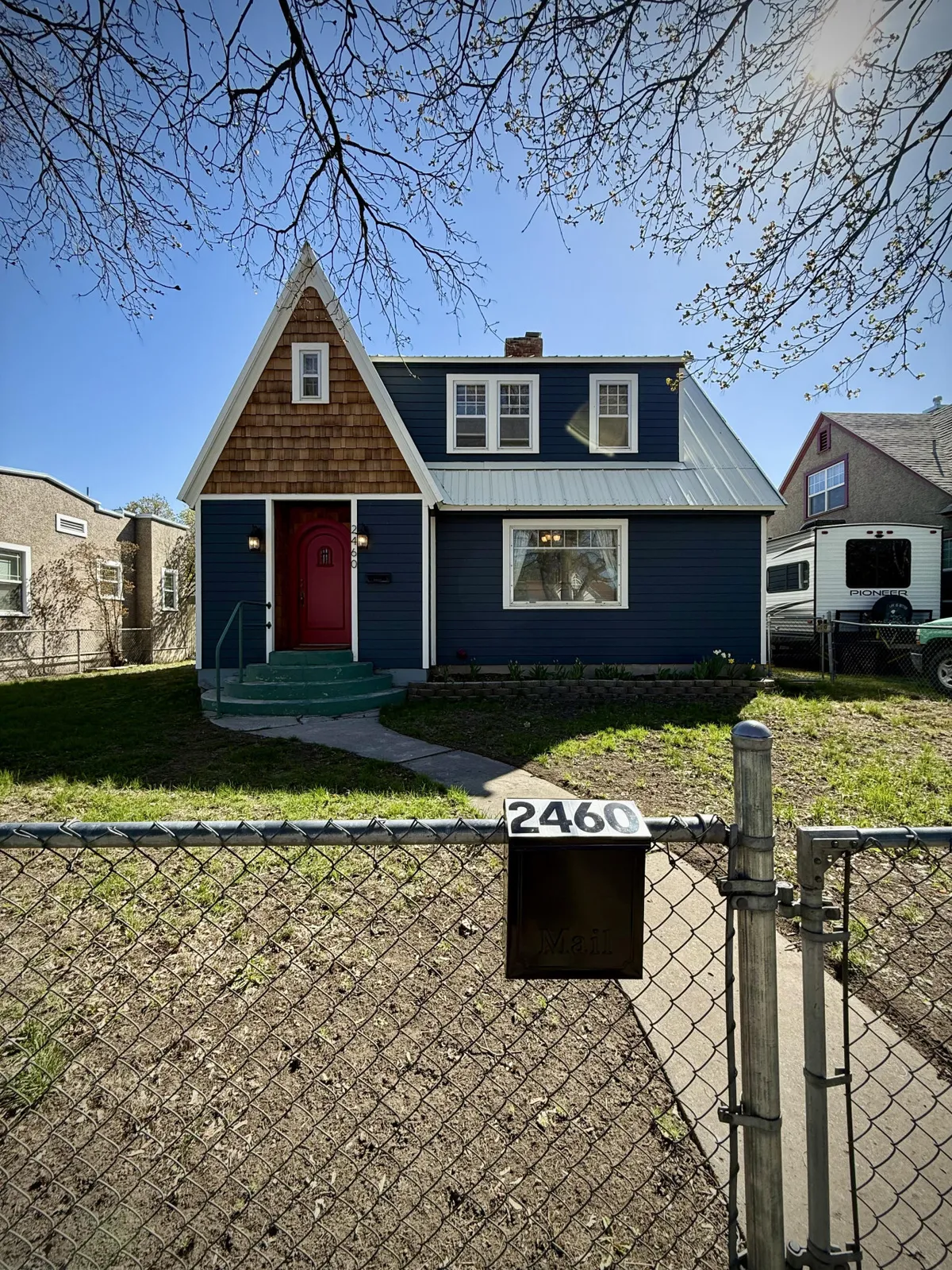 This image displays the inviting blue exterior of the house, highlighted by its unique roof design and vibrant red front door. The porch and yard offer space for families or groups to gather or unwind.