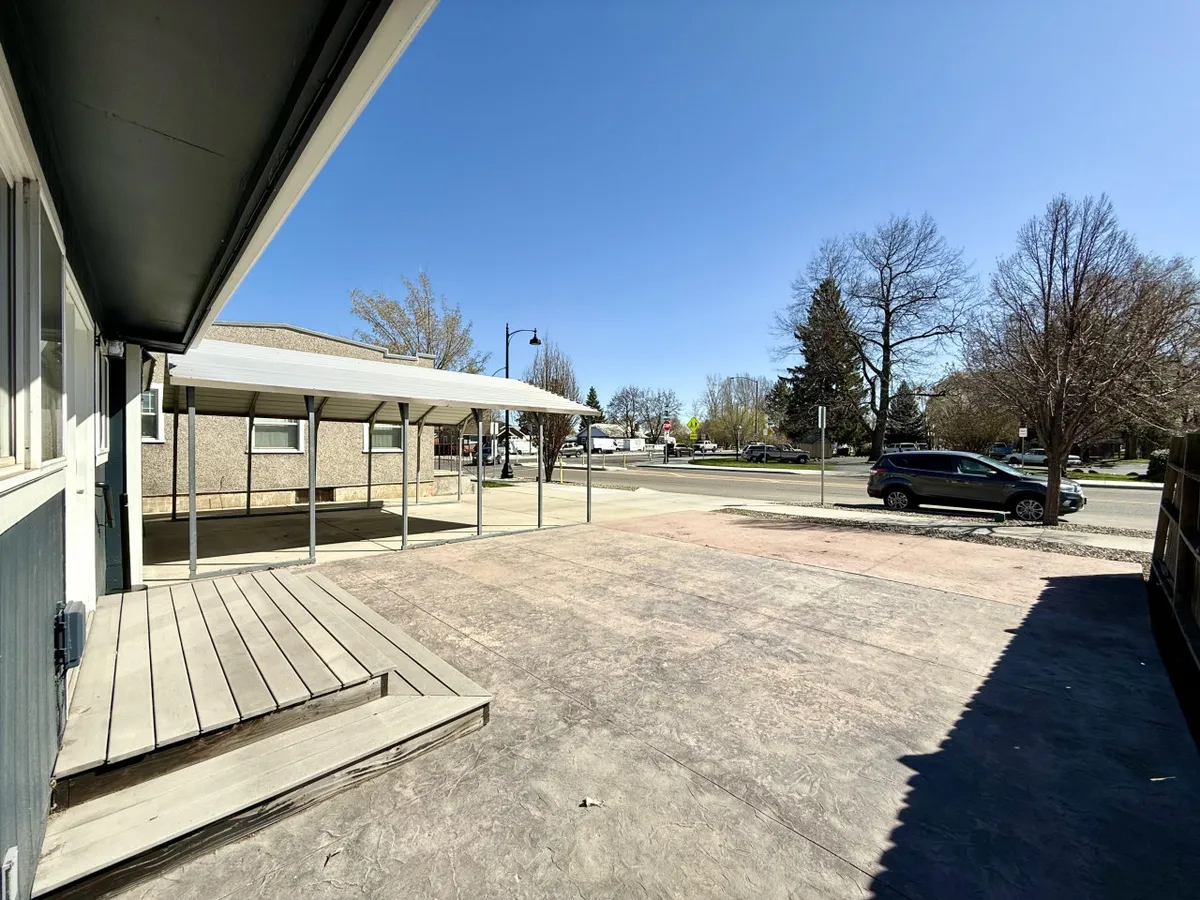 An exterior patio area with an overhead canopy, surrounded by trees and providing an open space for gatherings. The scene is set for casual outdoor activities and relaxation, suggesting easy access to nature and fresh air.