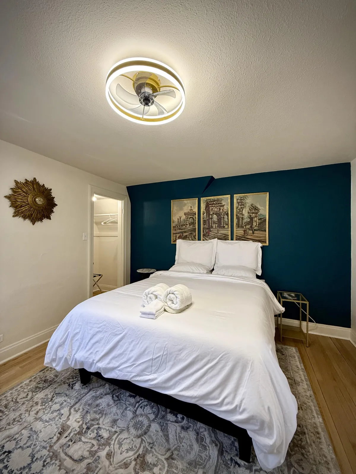 This image presents a tranquil bedroom featuring a bed with crisp white linens, decorative wall art, and a modern ceiling fan above. The composition exudes a calming, restful atmosphere, with natural light softening the room's edges, suggesting a retreat ideal for relaxation and unwinding after a long day.